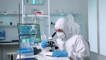 Scientist in ppe suit working in laboratory using modern microscope with slides. Team of chemists researcher examining virus evolution using high tech for vaccine scientific research against covid19 video