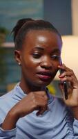 Vertical . Remote black employee speaking at phone while working at laptop late at night. Busy focused freelancer using modern technology network wireless doing overtime for job reading, searching taking break video