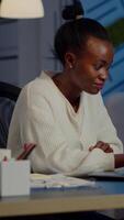 Happy african freelancer reading tasks on laptop working overtime in start up company office. Enthusiastic employee owerworking late night respecting deadline of financial project video