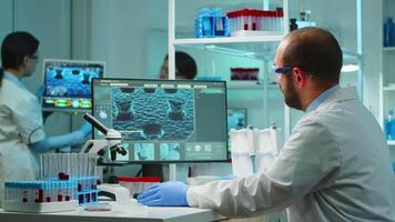 Worn out doctor typing on computer and looking exhausted at camera in equipped lab late at night. Medical chemists examining virus evolution using high tech for scientific research, vaccine development. video