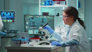 Microbiologist working late at night for new vaccine in modern laboratory looking at samples under microscope. Coworkers examining virus evolution using high tech and chemistry tools for research. video