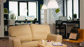 Interior of cozy light company room with small table and confortable couch, modern stylish chairs and desktop computer, all ready for employees. Empty spacious office of creative working space. video