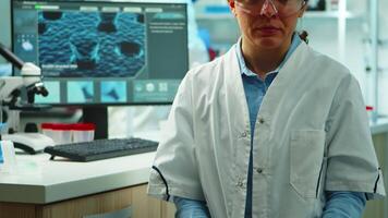 Close up of scientist nurse looking tired at camera sitting in modern equipped laboratory late at night. Team of specialists examining virus evolution using high tech for research, vaccine development video
