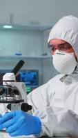 Vertical . Scientist in ppe suit placing a slide on specimen stage of a laboratory microscope making adjustments. Chemist in coverall working with various bacteria, tissue blood samples for antibiotics research video