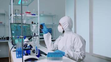 Scientist in ppe suit holding petri dish while studying virus samples in biotechnology lab typing on pc. Doctors examining vaccine evolution using high tech researching diagnosis against covid19 virus video