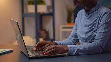 ocupado Preto empregado digitando em computador sentado em cadeira dentro moderno vivo quarto escritório atrasado às noite. africano empreendedor trabalhando dentro pessoal local de trabalho escrevendo em teclado olhando às Área de Trabalho video