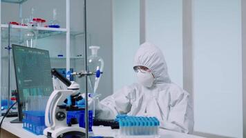 Medical scientist with coverall in laboratory room performs tests with blue liquid on test tube typing. Doctors examining vaccine evolution using high tech researching diagnosis against covid19 virus video