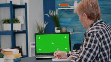 Elderly person reading on green screen, mock up, chroma key display of laptop, writing on notebook working from home. Senior woman watching at pc with isolated desktop, while man sitting on sofa video