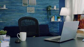 Pretty simple modern decor of cozy apartment with no people in it and television in background. Empty workspace of freelancer worker with laptop computer on desk and cup of coffee. video