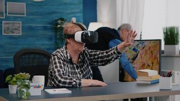 Retired woman experiencing virtual reality using vr headset in living room working from home. Old remote employee searching, analysing financial reports while elderly wife watching tv in background video