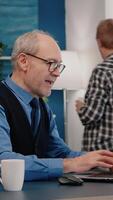 Vertical . Excited senior man feel ecstatic reading great online news on laptop working from home. Retired employee using modern technology reading typing, searching while senior wife sitting on couch video