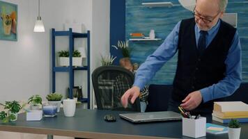 Senior remote businessman opening laptop and reading reports working from home drinking coffee. Retired man using modern technology analysing, searching info while wife sitting on couch reading a book video