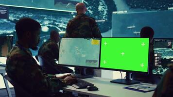 Intelligence analyst reviews ships activity next to an isolated mockup screen, following gps coordinates of vessels anchoring along the coastal ports. Army officer in monitoring room. Camera B. video