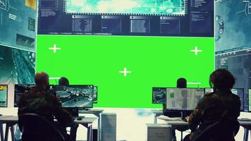 Diverse group of privates operating on a big screen isolated display, looks at a greenscreen and gathering intelligence to help with military operations in command center. Army facility base. Camera B. video