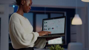 African freelancer typing on laptop late at night standing in start up business office late at night working. Busy employee using modern technology network wireless doing overtime for job searching video