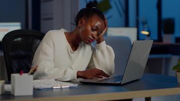 Exhausted african freelancer resting head on hand in front of laptop working overtime in start up company office. Stressed employee using modern technology doing overtime for deadline of project video