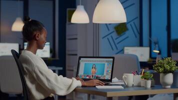 Dark skin freelancer retoucher woman working overtime on laptop with photo editing software. Professional graphic editor retouching photo of a client during night time in home office on performance pc video