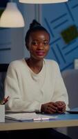 Portrait of business black woman looking at camera smiling raising head from laptop working in start-up financial company late at night. Focused employee doing overtime respecting deadline of project video