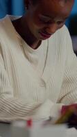 Close up portrait of business african woman smiling at camera after raising head from laptop sitting in startup company late at night. Focused employee doing overtime respecting deadline of project video