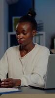 African manager woman using laptop and tablet in same time working overtime in business start-up office. Busy multitasking Busy employee analysing financial statistics overworking writing, searching. video