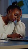 Exhausted african freelancer resting head on hand in front of laptop working overtime in start up company office. Stressed employee using modern technology doing overtime for deadline of project video