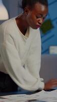 Stressed african manager woman working with financial documents checking graphs, holding papers, reading raports, standing at desk late at night in start-up office doing overtime to respect deadline. video