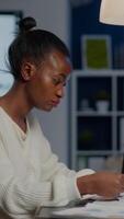Black manager analysing graphics and financial statistics from documents working overtime in front of laptop sitting in start-up business office. Focused employee respecting deadline of project video