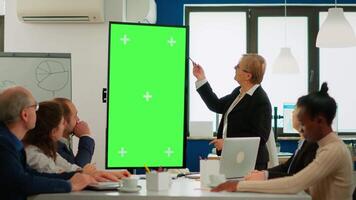 Diverse business team sitting at meeting table analysing financial statistics, looking at green screen display while senior leader explaning. Multiethnic workers planning project on chroma key desktop video
