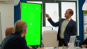 Young man leader of company presenting financial strategy using green screen mockup display in front of diverse team brainstorming. Manager explainig project showing monitor with chroma key desktop video