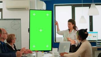 Young leader briefing diverse businessteam standing in front of meeting table analysing financial statistics, looking at greenscreen display. Multiethnic workers planning project on chroma key desktop video