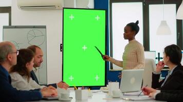 Diverse woman standing in start up office discussing strategy with green screen monitor in front of business partners. Manager explaining to multiethnic team project chroma key display mock up desktop video