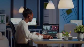 Black editor working overtime at new project editing audio film montage sitting in start-up business office. Woman content creator using professional laptop, modern technology, network wireless video