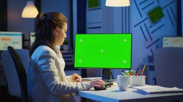 Woman looking at computer with chroma key during night time in start up business office working overtime. Freelancer watching desktop monitor mockup display with green screen, typing writting video