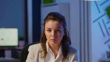 Tired woman manager raising head looking at camera sighing after typing on laptop, working late at night in start-up business office. Focused employee using technology network wireless doing overtime video