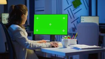 Businesswoman looking at green screen monitor of computer sitting at desk in business office late at night. Freelancer watching desktop monitor display with green mockup, chroma key working overtime. video