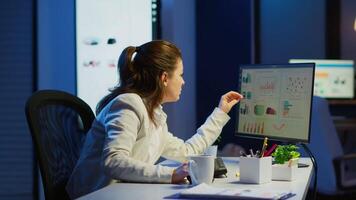 Focused tired entrepreneur checking graphics from laptop writing on notebook working from business office overtime. Busy employee using modern technology network wireless reading typing, searching video