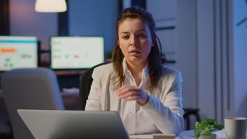 Exhausted businesswoman typing an email late at night and looking tired in camera sighing resting head in palm. Focused employee using technology network wireless doing overtime for job video