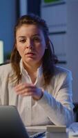 Vertical . Exhausted businesswoman typing an email late at night and looking tired in camera sighing resting head in palm. Focused employee using technology network wireless doing overtime for job video
