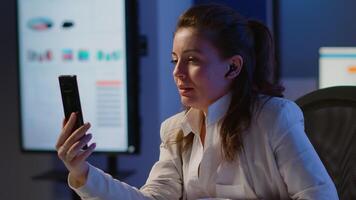 Entrepreneur having virtual meeting using smartphone with wireless headphone sitting at desk in workplace. Freelancer working with remotely team chatting virtual online conference, using internet video