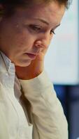 Vertical . Close up of stressed busy woman with headache working from business office late at night. Tired focused employee using modern technology network wireless doing overtime for job checking reports video