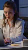 Vertical . Business woman working overtime to respect deadline of project sitting in business office typing on laptop late at night. Busy focused employee using modern technology network wireless searching video