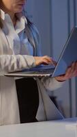 Vertical . Exhausted business woman holding laptop, typing and sighing looking at camera standing in start-up company late at night. Employee using technology network wireless doing overtime for job reading. video