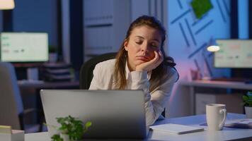 Tired remote woman napping on chair waking up working on laptop in start up company office late at night. Busy employee using modern technology network wireless doing overtime closing eyes sleeping. video