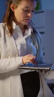 Vertical . Manager woman holding laptop, typing and looking satisfied at camera standing in start-up company late at night. Focused employee using technology network wireless doing overtime for job reading. video