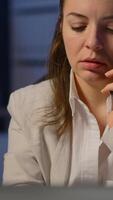 Vertical . Tired freelancer woman having conversation on phone while working exhausted in business office late at night doing overtime. Focused employee using modern technology network wireless overworking video