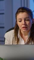 Vertical . Business woman using wireless headphone duing conference working overtime from start-up office in front of laptop. Lady using modern technology network talking on virtual meeting at midnight video