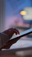 Vertical . Close-up photo of woman hands typing on tablet checking financial graphs standing in start-up office late at night. Businesswoman using social network, texting and blogging working overtime for job video