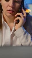 Vertical . Concentrated businesswoman during phone call late at night working from business office discussing with coworker. Busy employee using modern technology network wireless doing overtime for job talking video