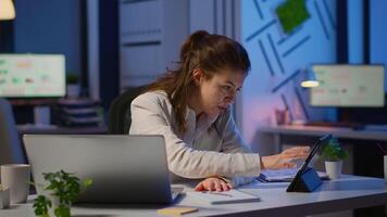 Manager woman using laptop and tablet in same time working overtime in business start-up office. Busy multitasking employee using modern technology network wireless overworking writing, searching. video