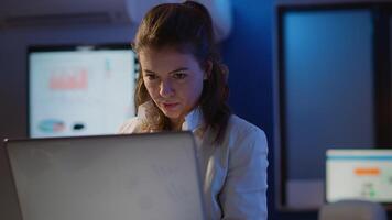 Freelancer typing on laptop late at night standing in start up business office late at night working. Busy focused employee using modern technology network wireless doing overtime for job searching video